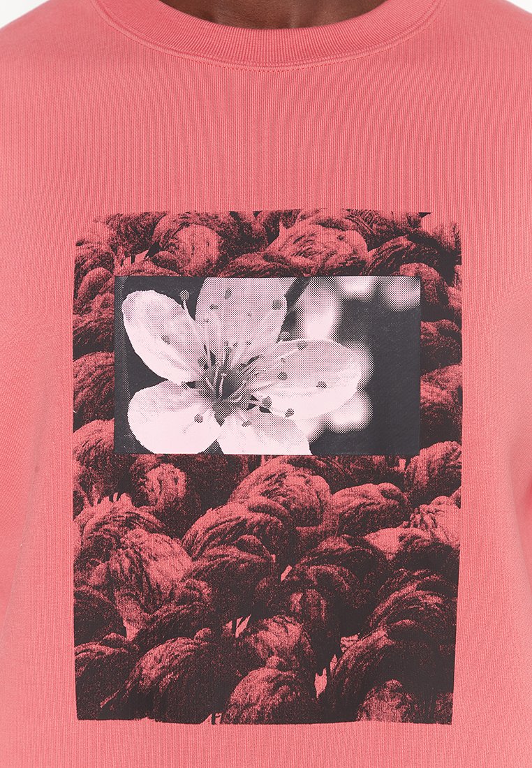 Różowy sweatshirt o prążkowanej fakturze z centralnym czarno-białym graficznym wzorem kwiatowym na kontrastowym tle.