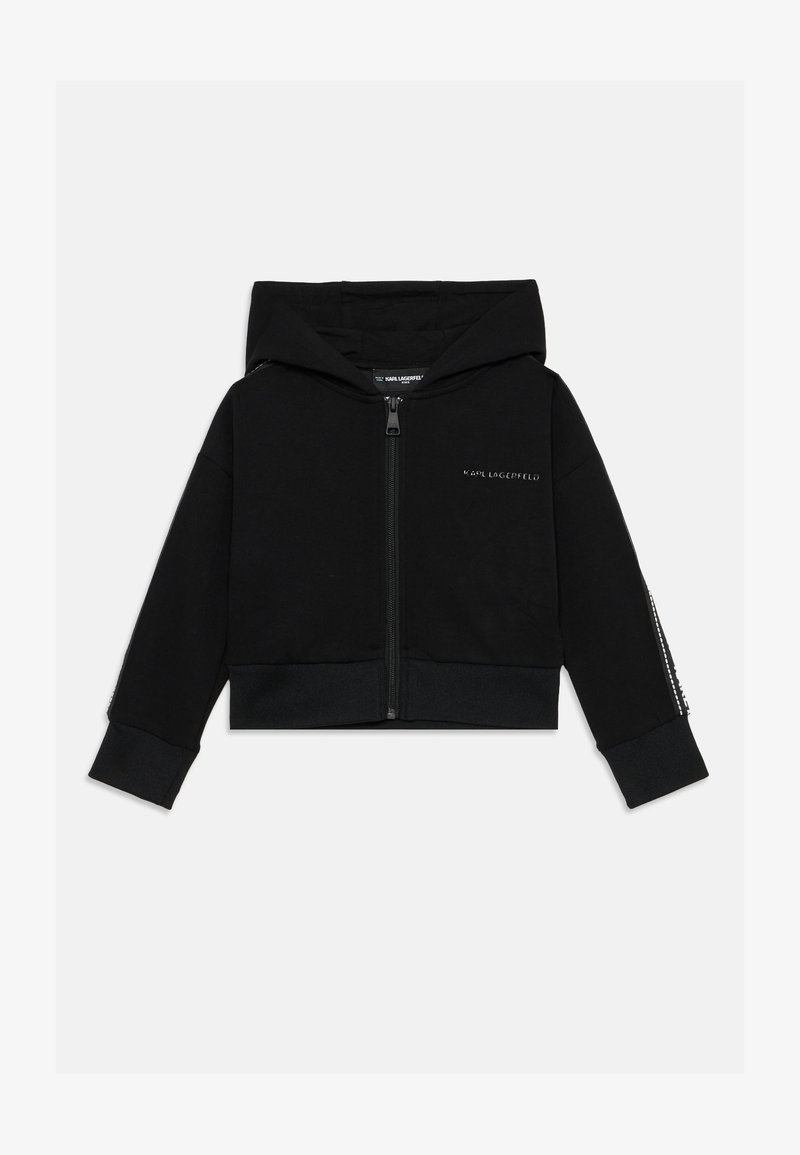 Sudadera corta negra fabricada con tela suave. Presenta una cremallera frontal, capucha y dobladillo acanalado. La manga izquierda tiene detalles decorativos.