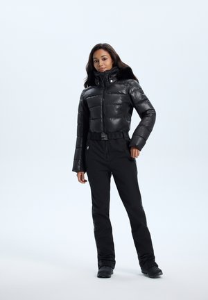 Black puffer jacket with a high collar and zipper, paired with black pants. The fabric appears glossy, with a belted waist detailing.