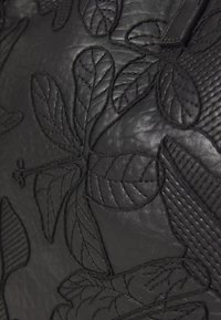 Superficie de cuero negro con patrones de hojas y botánicos en relieve, con un acabado texturizado y suave. Incluye detalles de costura sutiles.