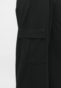 Zwarte stoffen jas met een opvallende zak met flap op de linker mouw, gladde textuur en strakke lijnen, gesneden in een modern ontwerp.