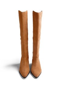 Un par de botas altas de gamuza color beige con puntas afiladas y suelas negras, de pie sobre un fondo blanco.