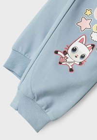 Jasnoniebieska bluza z kapturem z rysunkiem kota w stylu kreskówkowym, z wyrazistymi oczami, różowymi akcentami oraz ściągaczami. Miękka, gładka w dotyku.