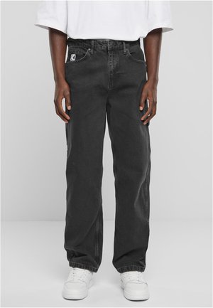 Black denim pants with a straight-leg fit, featuring five pockets and a branded tag on the front. Worn with white sneakers.