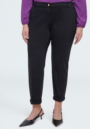 Vrouw draagt zwarte cropped broek met opgerolde pijpen, gecombineerd met zwarte slingback pumps met puntige neus en een paarse blouse met lange mouwen.