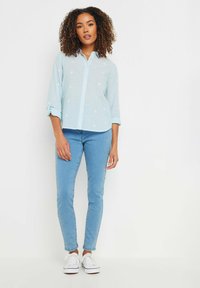 Light blue button-up shirt with embroidered flowers, rolled sleeves over blue skinny jeans and white sneakers. Smooth fabric with a textured pattern.
