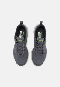 Graue Sportschuhe aus atmungsaktivem Mesh-Material, mit Schnürdesign, gepolstertem Schaft und grünen Akzenten an der Seite.