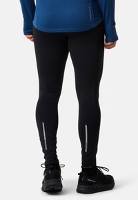Svarta atletiska leggings med reflekterande detaljer, som har en åtsittande design och elastiskt material. Bärs med svarta sportskor.