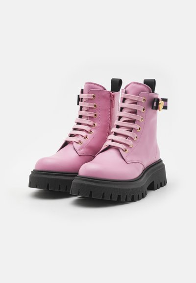 Botas de cuero rosa con cordones, suelas gruesas de goma negra, cremalleras laterales, tirador negro y un charm en forma de corazón dorado en la correa del tobillo.