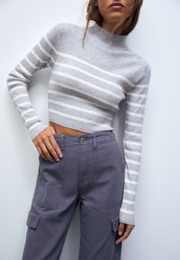 Grå ribbet kort sweater med hvide striber, med høj hals og lange ærmer, parret med højtaljede grå cargo bukser.