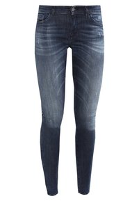 Jeans ajustados en denim azul oscuro, con un lavado desgastado y ligero desgarro. Diseño estándar de cinco bolsillos y cierre de cremallera con botón.