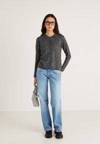 Jersey gris de punto con cuello, cierre de botones y detalle de rayas verticales. Combinado con vaqueros azul claro y zapatos negros, sosteniendo un bolso gris.