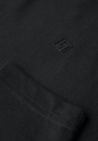 Czarna tkanina bawełniana z subtelnym, wytłoczonym logo. Design jest minimalistyczny, z czystymi szwami i gładką fakturą.