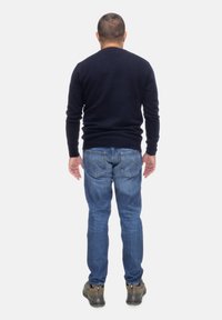 Granatowy sweter dziergany, niebieskie dżinsy, brązowe buty trekkingowe. Widok z tyłu ukazuje dopasowany krój, gładką teksturę i swobodny styl.