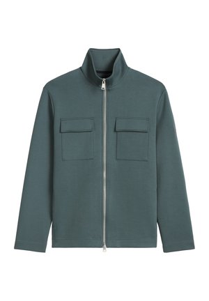 Donkergroene lange mouw ritsjas met hoge kraag en twee vierkante klepzakken op de borst tegen een witte achtergrond.