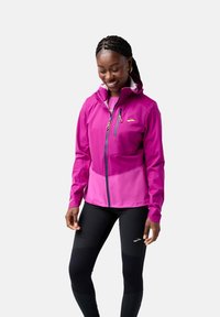 Roze softshell jack met capuchon, ritszakken en contrasterende lichtere secties. Draag het met zwarte leggings met textuurelementen.