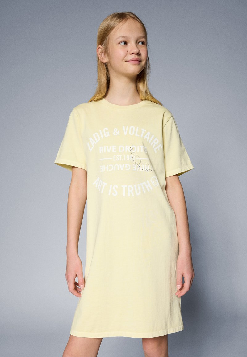 Vestido de camiseta de algodón amarillo con mangas cortas, que presenta texto impreso blanco y un acento de strass. Textura suave y corte relajado.