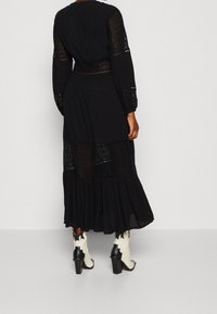 Abito maxi nero con maniche lunghe, dettagli in pizzo e orlo a strati. Abbinato a stivali da cowboy con tacco bianchi e neri.