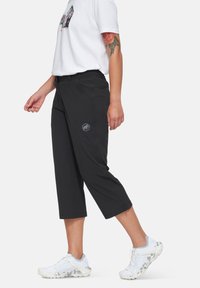 Μαύρο καπρι παντελόνι με λεία υφή, διαθέτοντας λεπτομέρεια λογότυπου στο μηρό. Συνδυασμένο με λευκά αθλητικά παπούτσια και μπλούζα με γραφικό σχέδιο.