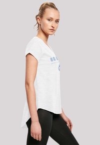 White short-sleeve T-shirt with a slightly longer back, featuring blue text and graphic design. Paired with black leggings.