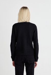 Pulover negru din tricot cu nervuri, cu mâneci lungi, gât rotund și croială lejeră. Țesătură texturată vizibilă pe spate și la mansete. Design simplu.