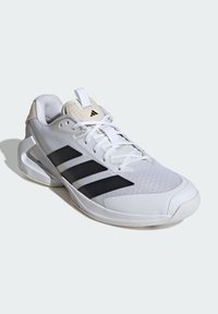 Zapatillas deportivas con una parte superior de malla blanca, acentos en negro con tres franjas y una suela de goma texturizada. Presenta una punta reforzada y un collar acolchado.