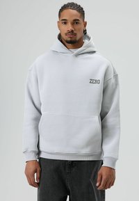 Lichtgrijze hoodie van een katoenmix, met een voorzak en een "ZERO"-logo in een donkere textuur op de linkerborst.