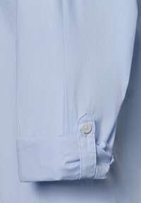 Camicia a maniche lunghe blu chiaro con polsini abbottonati e bordo arrotondato, realizzata con un tessuto leggermente texturizzato.