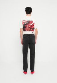 Λευκό γραφικό μπλουζάκι με σχέδιο κόκκινου καθίσματος αυτοκινήτου στην πλάτη, σε συνδυασμό με μαύρα τζιν και κόκκινα αθλητικά παπούτσια. Ορατό κείμενο στο σχέδιο του μπλουζιού.