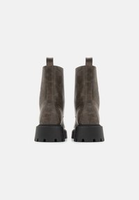 Brune syntetisk lær ankelstøvler med en kraftig svart gummisåle og løkker bak, med en glatt tekstur og stilrent design.