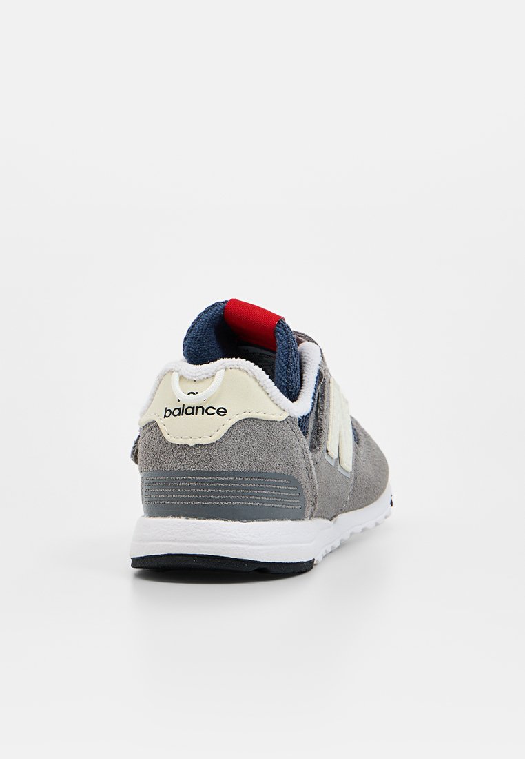 Baskets en suède gris avec semelle blanche, dotées d'une languette bleu marine, d'un accent rouge au talon et d'un logo blanc sur un panneau beige.