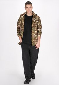Kamouflagejacka i nyanser av grönt och brunt, svart t-shirt, svarta vida byxor och svarta stövlar. Avslappnad streetwear-outfit.