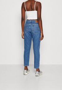 Jean en denim bleu clair avec une taille haute, une coupe droite et cinq poches. Associé à un top court blanc et des baskets argentées.