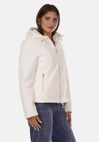 Giacca bianca con cappuccio, dotata di zip frontale, due tasche laterali e cordini regolabili sul cappuccio. Tessuto liscio e design aderente.