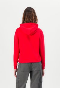 Sarkans kapucis džemperis ar brīvu piegriezumu, ribinātām aprocēm un apakšmalu. Apvienots ar pelēkiem cargo biksēm, kas aprīkotas ar kabatām un kontrastējošu šuvju šūjumu.