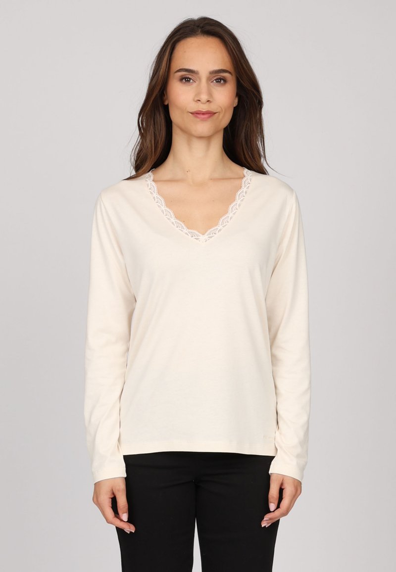 Haut crème à manches longues avec un décolleté en V, orné d'une délicate bordure en dentelle. Tissu doux au toucher lisse. Associé à un pantalon noir.