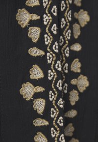 Tessuto nero con complessa ricamo dorato che presenta motivi a cuore e a diamante, mettendo in mostra una delicata texture e maestria artigianale.