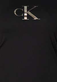 Czarna koszulka z srebrnym metalicznym logo "cK". Gładki materiał, dopasowany krój, krótkie rękawy i okrągły dekolt.
