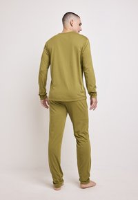 Olive green long-sleeve top and matching pants made of soft fabric, featuring a relaxed fit and simple design. Barefoot, viewed from behind.