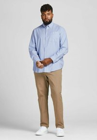 Camisa azul clara de botones con un bolsillo en el pecho, combinada con pantalones beige y zapatillas blancas, con un ajuste relajado y una textura suave.