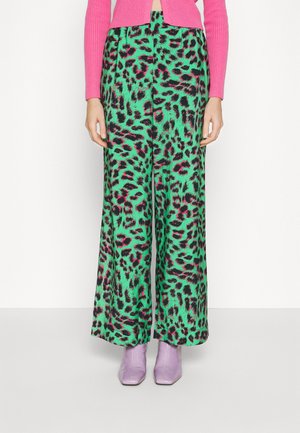 Mujer con pantalones anchos verdes con estampado de leopardo negro y rosa, suéter rosa acanalado y botines de punta cuadrada en lavanda.