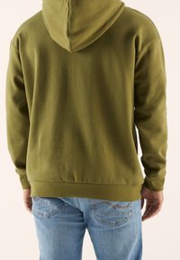 Felpa verde oliva con cappuccio regolabile, polsi e vita a costine, abbinata a jeans in denim azzurro chiaro con un semplice motivo di cucitura.