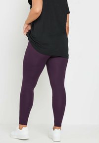 Leggings morados con una textura suave, forma ajustada y cintura alta, combinados con una camiseta negra de corte holgado y zapatillas blancas.