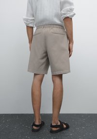 Beige shorts i en afslappet pasform med elastisk talje, der har to baglommer og en opkrøllet kant, parret med sorte sandaler.