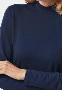 Marineblaue Langarmoberteil mit hohem Kragen, glatter Textur und taillierter Silhouette. Verfügt über angenähte Bündchen und minimale Details.