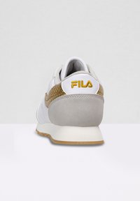 Baskets blanches et grises avec un accent texturé en or et imprimé serpent, dotées d'un col rembourré et du logo Fila sur le talon.