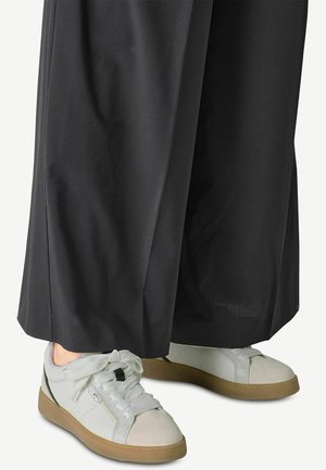 Sneaker bianche con accenti beige, punta rotonda e lacci larghi. Indossate con pantaloni neri larghi, che mostrano una texture di tessuto liscia.