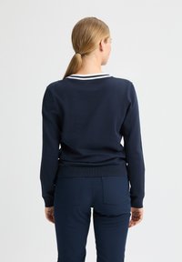 Navy sweater met een getailleerd ontwerp, ronde hals en gestreepte witte accenten op de kraag. Gemaakt van zachte gebreide stof.