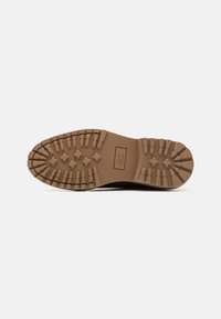 Brown rubber shoe sole with a textured, patterned surface featuring star-shaped grips for traction. Rectangular branding label present.