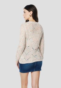 Kötött pulóver texturált, nyitott mintával, többszínű fonalból, hosszú ujjakkal és kerek nyakkivágással, farmer miniszoknyával párosítva.